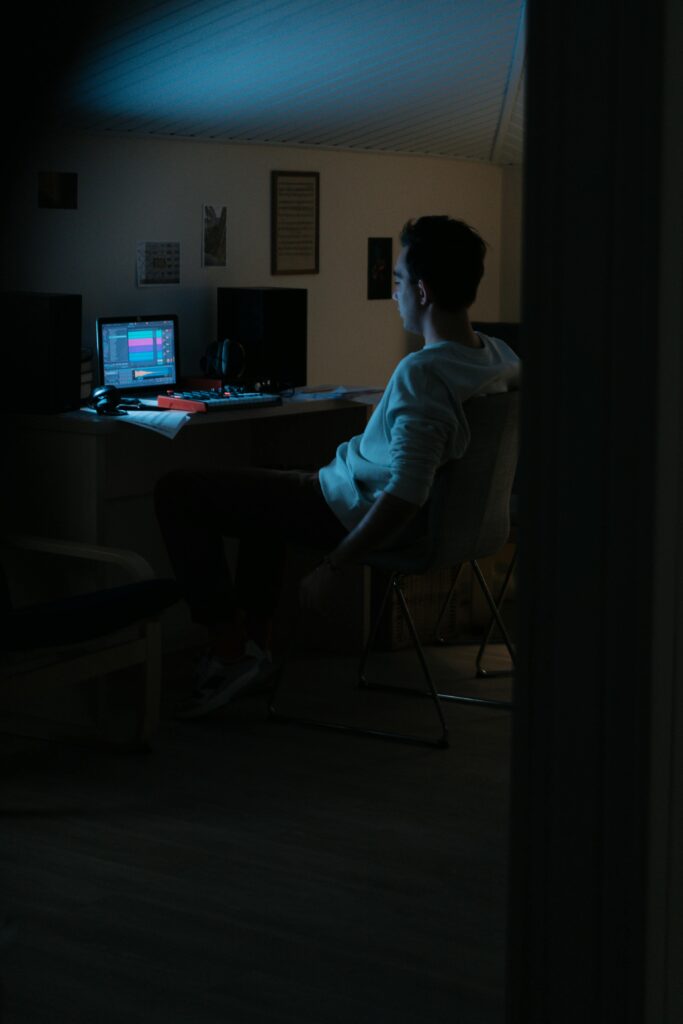 Young musician composing music on a laptop in a dimly lit home studio.